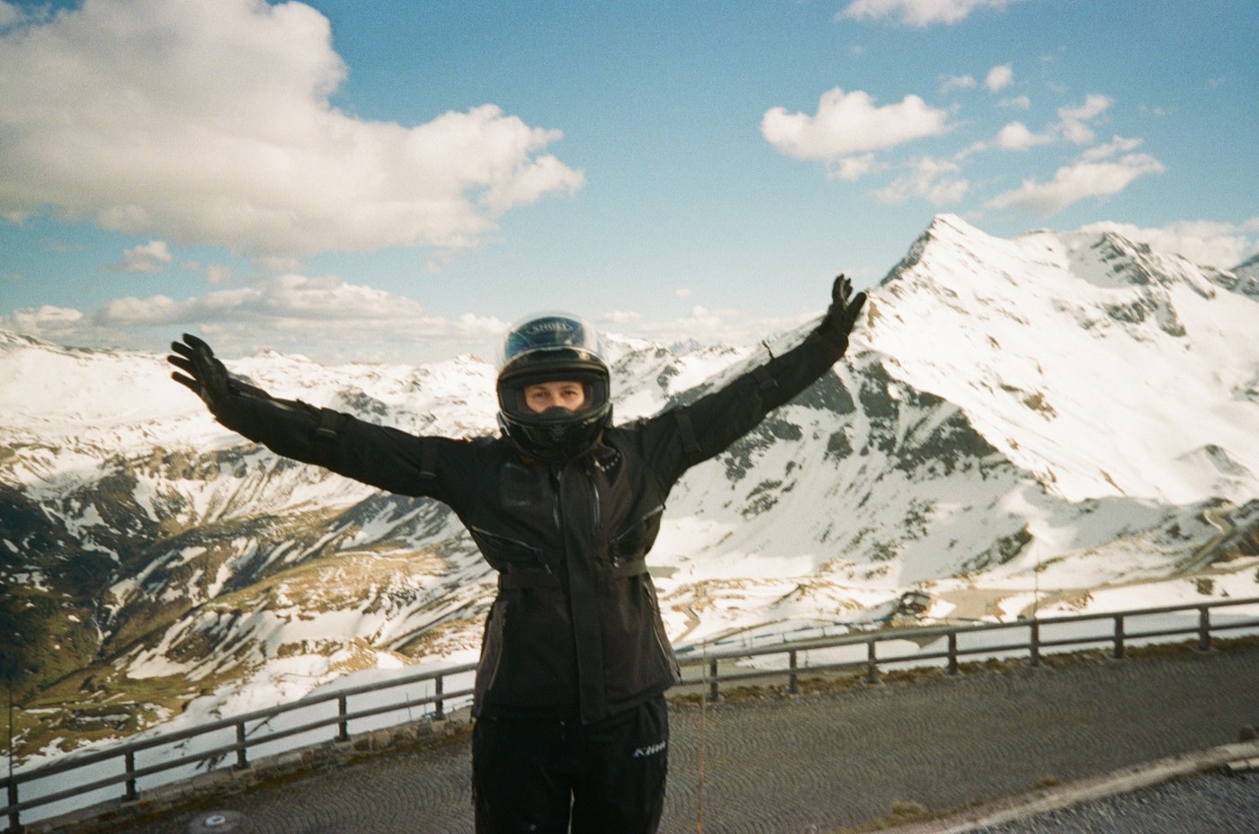 Marc mit ausgebreiteten Armen in Motorradmontur vor schneebedeckten Alpengipfeln
